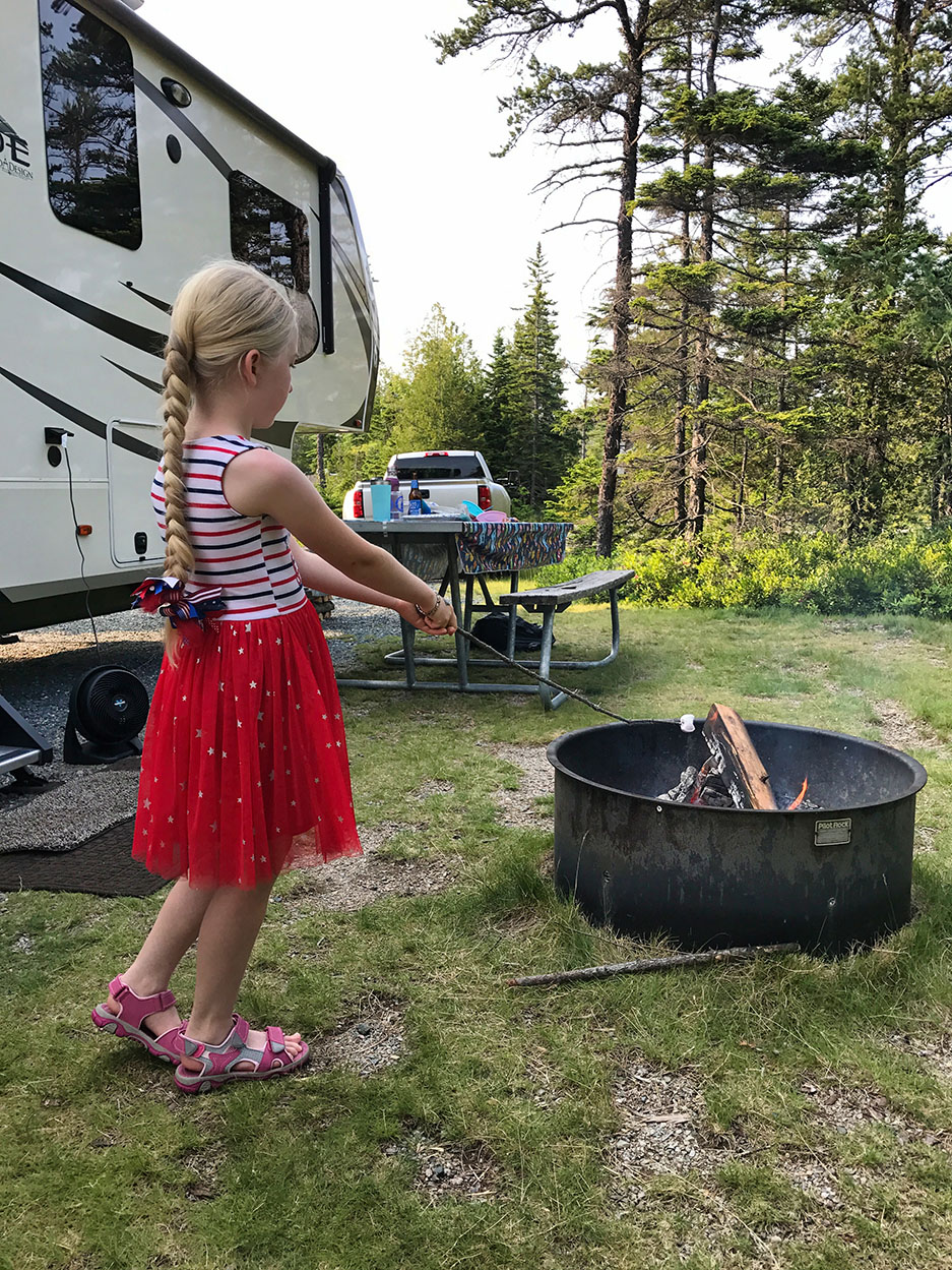 girl roasting marshmallows on a fire near an RV : full-time RV living with kids